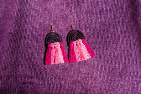 A pair of stylish and fashionable macrame earrings with a rainbow shape and tassel detail on a purple fabric background.の写真素材