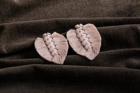 Handmade macrame palm leaf decorations resting on a textured dark brown fabric background, showcasing natural tones.の写真素材