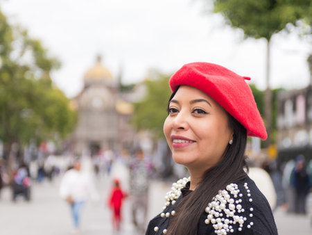 Outdoor portrait of a smiling woman wearing a red beret and a sweater embellished with pearlsの写真素材