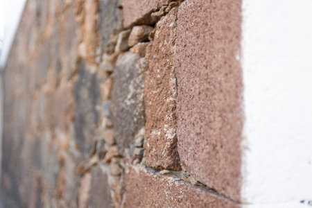 Close-up of a rustic stone wall with roughly hewn stones in reddish-brown tones. Angled view.の写真素材