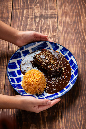 Traditional mole dish with rice on a blue patterned plate being held by two handsの写真素材