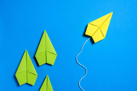 A yellow paper airplane moves along its own path while three green paper airplanes remain together on a bright blue background.