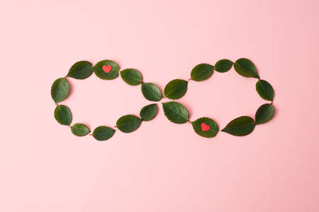 Infinity symbol made with green leaves and red hearts on pastel background. Concept of eternity....