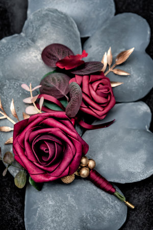 The groom's red material rose boutonniere with gold leaf and green stem laying on top of grey stone...