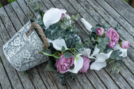 A beautiful silver vintage floral decorative bucket full of cascading pink and ivory flowers against a rustic wood background.の写真素材