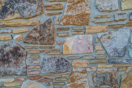 Colorful random rocks stacked and cut into a pattern in between mortar with different shapes and sizes forming a wall on a building outdoorsの写真素材