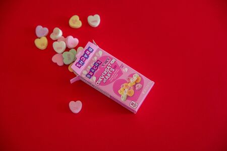 An opened box of Brach's Valentine candy hearts spilled out onto a red background