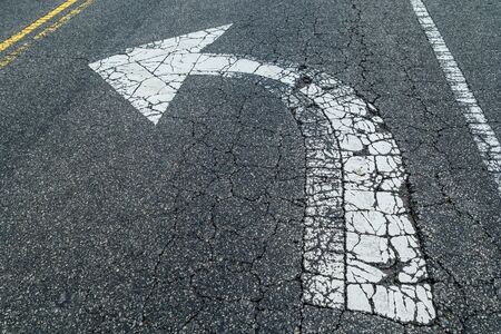 A left turn only arrow painted white on the asphalt cracked and worn away by traffic on the street...