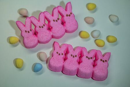Arrangement of bright pink marshmallow bunny peeps with assortment of colorful candy eggs surrounding on a white backgroundの写真素材