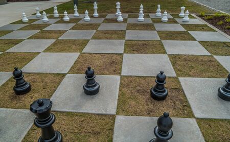 Looking downward at a giant outdoor chess set on cement and grass squares to move the large game piecesの写真素材