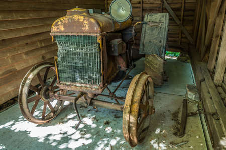 A 100 year old antique tractor with crank start crumbling and rusting away in a shed obsolete farm equipmentのeditorial素材