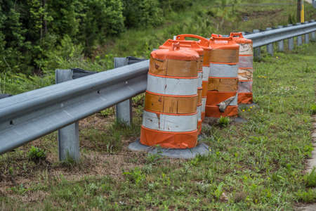 Several construction barrels tattered and grungy left abandoned alongside the guardrail by the...