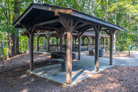 A picnic pavilion with a large grill for big gatherings under a shelter with a water spigot and garbage cans and several tables in the wooden structure outdoors in the parkの写真素材