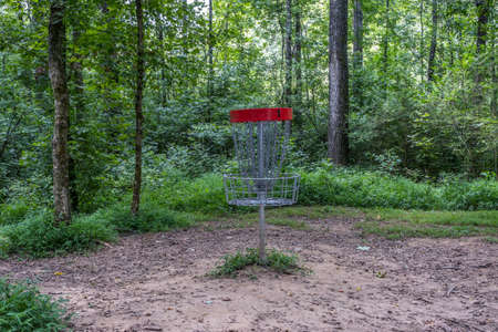 Disc golf basket with chains for catching the flying disc in the woodlands in a rustic setting on a course in the park in summertimeの写真素材