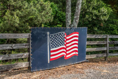 American flag painted on a large piece of metal bolted to a fence outdoors along the roadway showing...