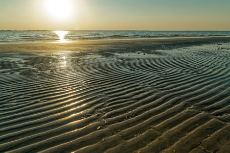 Bright sunlight reflecting across the rippled beach during setting with the ocean in the background