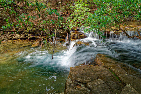 Side view of a small cascading waterfall long exposure spilling into the creek on a sunny day in early springtimeの写真素材
