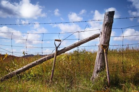 Shovels leaning near the fence against clouds and blue skyの写真素材