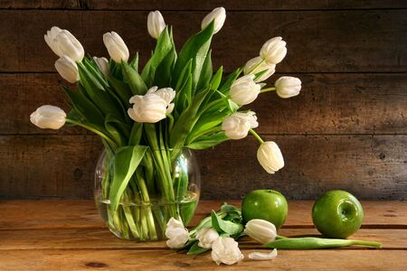 White tulips in glass vase with rustic wood backgroundの写真素材