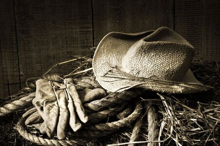 Straw hat with gloves on a bale of hay in barn/BWの写真素材