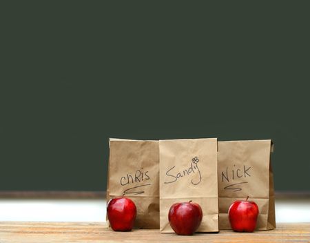 Lunch bags on desk with red apples in front of green chalkboardの写真素材