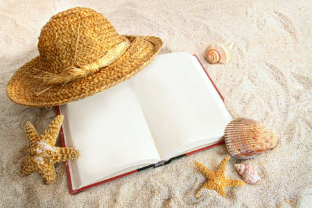 Book with straw hat and seashells at the beachの写真素材
