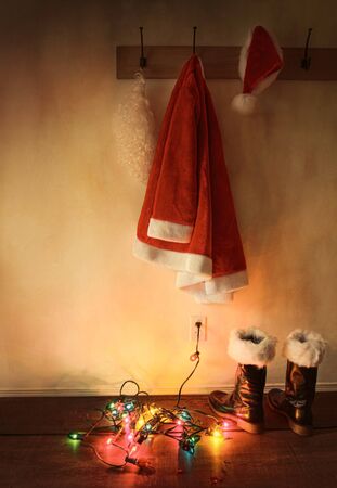 Santa costume hanging on coat hook with christmas lights on floorの写真素材