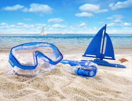Goggles and toy sailboat in sand at the beach scene の写真素材