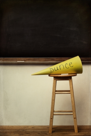 Yellow dunce hat on stool with chalkboard in backgroundの写真素材