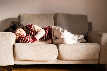 A young brunette woman takes a siesta on her grey sofa in her living room at home