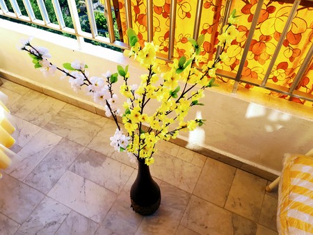 A photo showing a vase filled with artificial yellow and white flowers, that is sitting on the floor of a balcony.の写真素材