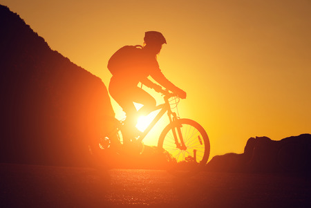 silhouette of a young woman on a bicycle at sunsetの写真素材