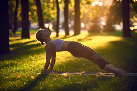 Young woman practicing yoga, stretching in Purvottanasana exercise - Upward Plank pose in the park at sunsetの写真素材