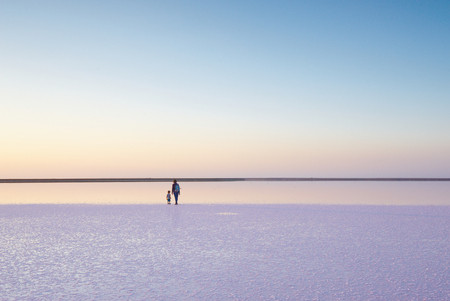 Mother and child walking on a salt and brine of a pink lake, colored by microalgae Dunaliella salinaの写真素材