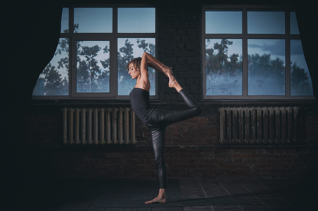 Beautiful sporty fit yogi woman practices yoga asana Natarajasana - Lord Of The Dance pose in the dark hallの写真素材