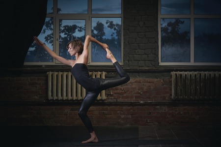 Beautiful sporty fit yogi woman practices yoga asana Natarajasana - Lord Of The Dance pose in the dark hallの写真素材