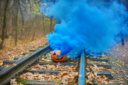 Smiling halloween pumpkin with bright blue smoke on the rails in the forestの写真素材