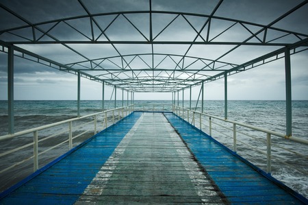 Old wooden jetty, pier, during storm on the sea. Dramatic sky with dark, heavy clouds. Vintageの写真素材