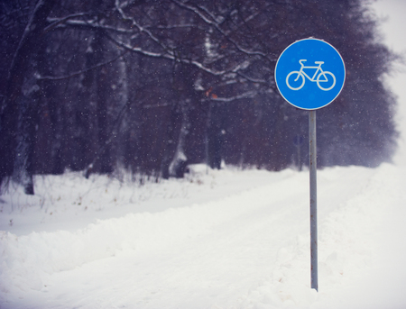 Cycle lane sign covered with snow against a dark forest.の写真素材