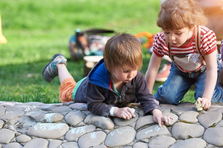 Little boy and girl drawing with sidewalk chalk in the parkの写真素材