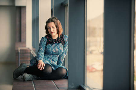 portrait of a young dreamy woman sitting on the window sillの写真素材