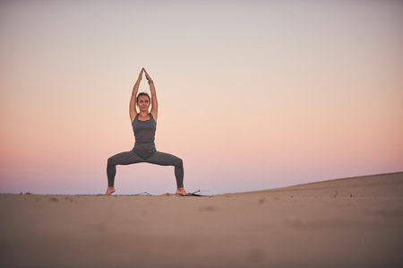 Beautiful young woman practices yoga asana Stupasana in the desert at sunset.の写真素材