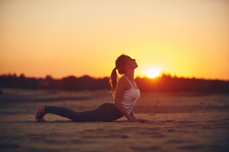 Beautiful young woman practices yoga asana Urdhva Mukha Svanasana - upward facing dog in the desert at sunset.の写真素材