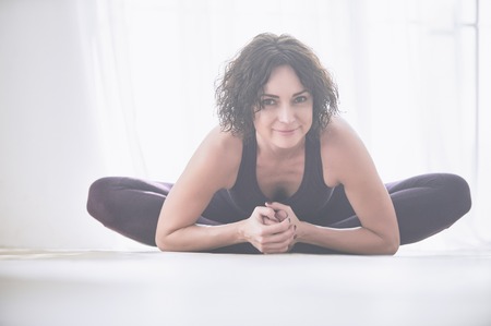 Beautiful young woman practices yoga asana Baddha Konasana - bound angle pose in the light yoga studioの写真素材