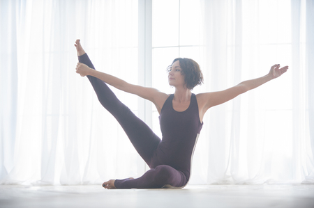 Beautiful young woman practices yoga asana in the light yoga studioの写真素材