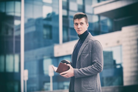 Young business man with notepad and mobile phone near of modern building.の写真素材
