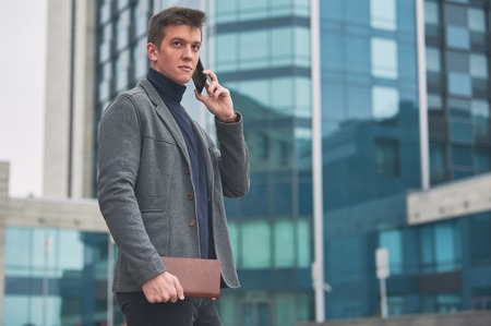 Young business man with notepad and mobile phone near of modern building.の写真素材