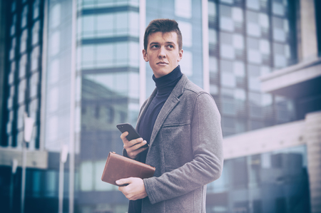 Young business man with notepad and mobile phone near of modern building.の写真素材