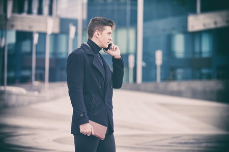 Young business man with notepad and mobile phone near of modern building.の写真素材