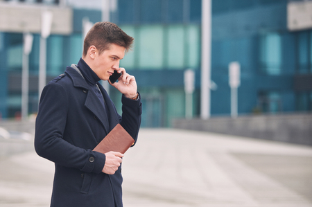 Young business man with notepad and mobile phone near of modern building.の写真素材